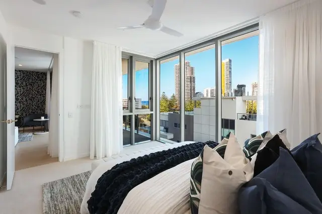 Master bedroom with floor-to-ceiling windows framing high-rise views and layered cream-and-navy linen