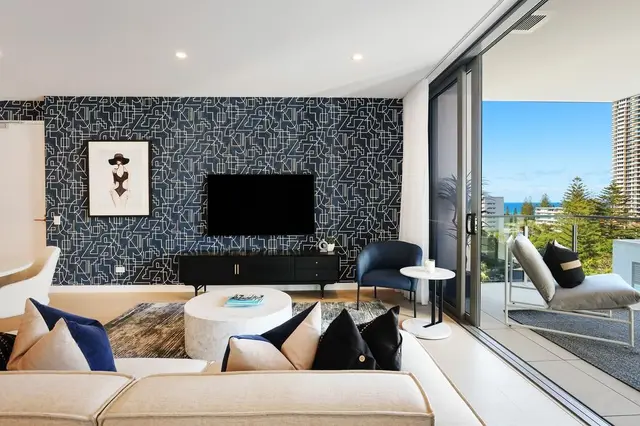 Living room with navy geometric feature wall, cream sofa, blue armchair and ocean-view balcony