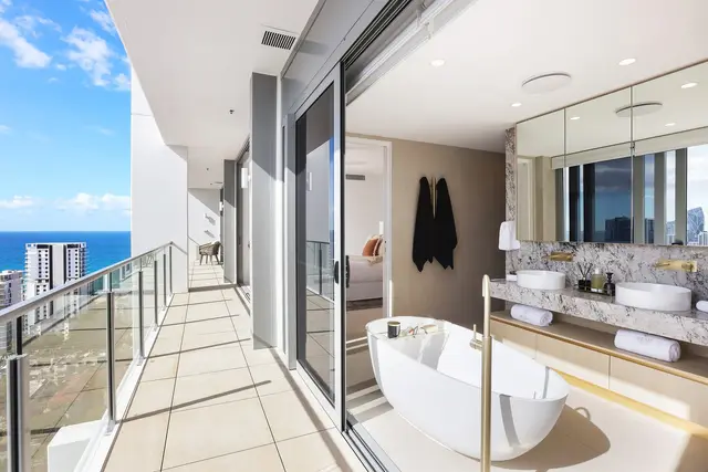 Ensuite with freestanding oval bath, veined marble vanity, twin basins and brass tapware beside the balcony