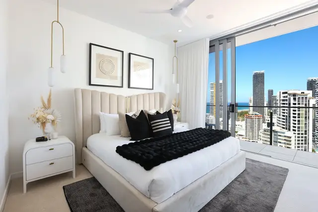 Bedroom with crisp white bedding, black studded cushions, smoked-glass pendants and wall-mounted television