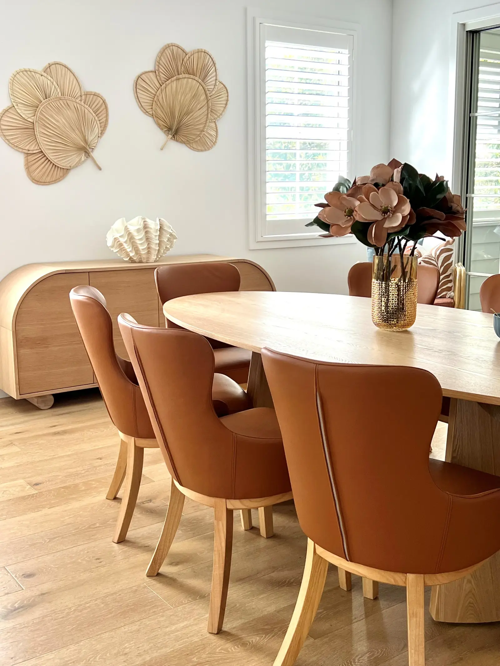 Dining area with oval oak table, tan leather wingback chairs and palm fan wall art