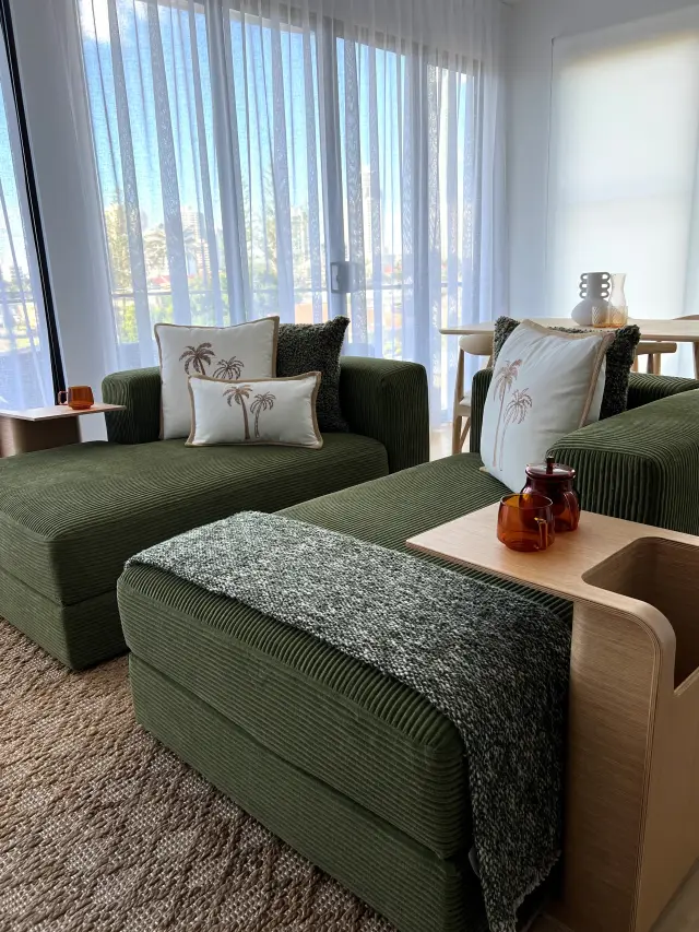 Family room with olive corduroy modular sofa, palm cushions and sheer curtains