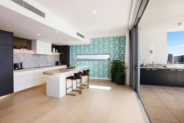 Kitchen with stone island, fluted white base, brass bar stools and palm-print feature wallpaper