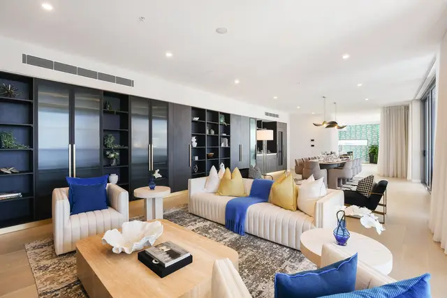 Living room with cream channel-tufted sofas, blue and mustard cushions and dark glass-fronted shelving