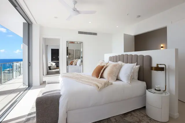 Master bedroom with grey scalloped headboard, layered neutral linen and floor-to-ceiling ocean views