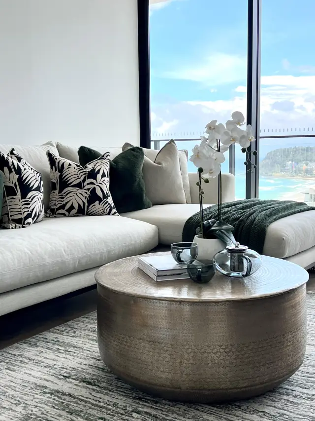 Media room with cream sofa, deep green and botanical cushions, hammered brass coffee table and ocean views