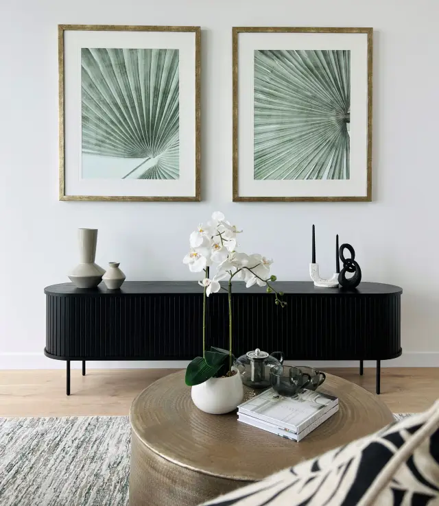 Black fluted entertainment unit with palm frond diptych, ceramic vessels and sculptural accents