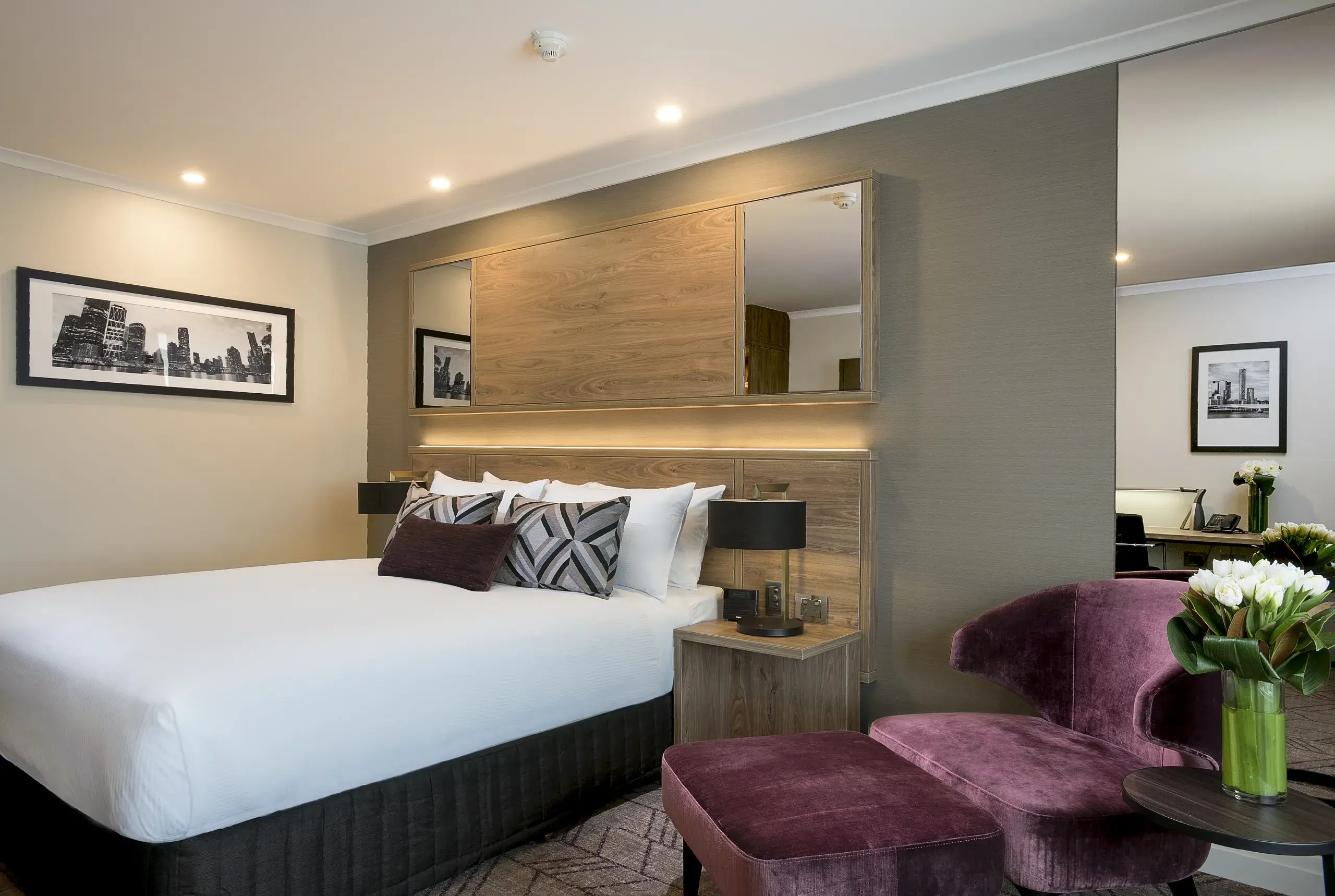 Hotel guest room at Rydges South Bank with a king bed, backlit timber headboard joinery and a plum velvet armchair