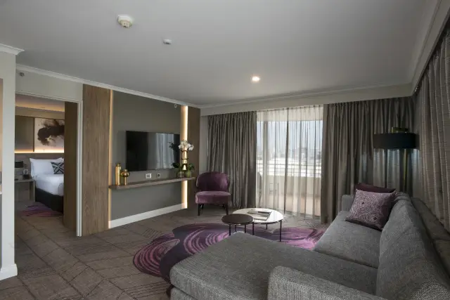 Open-plan suite showing the living area, wall-mounted TV joinery and connecting bedroom