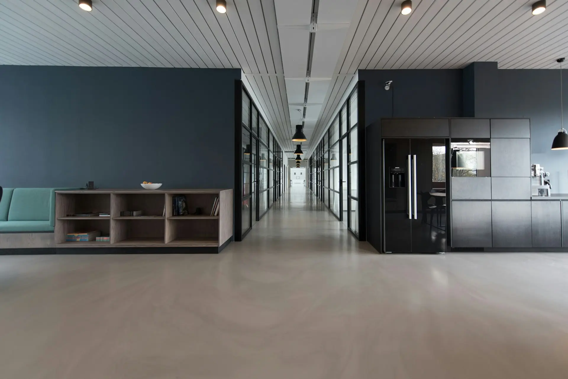 A commercial office interior with glazed partition walls, a polished concrete floor and a built-in kitchen and banquette