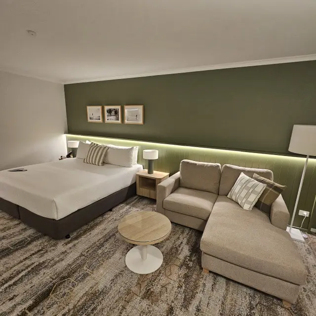 Guest room furnished with a taupe chaise sofa, round coffee table, framed coastal artwork and scatter cushions