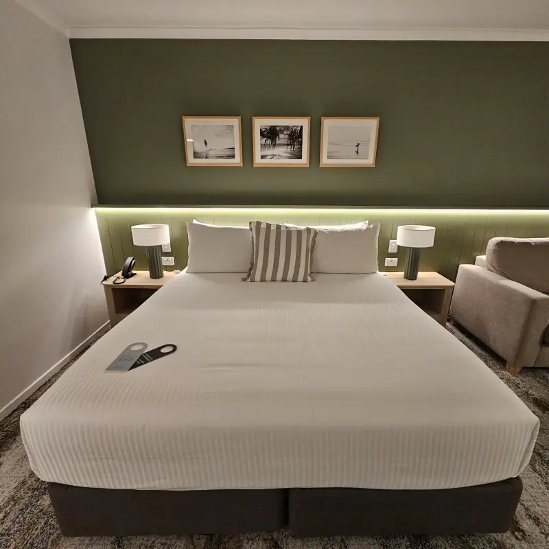 Rydges Port Macquarie king guest room furnished with a taupe sofa, framed black-and-white coastal artwork triptych and striped scatter cushion