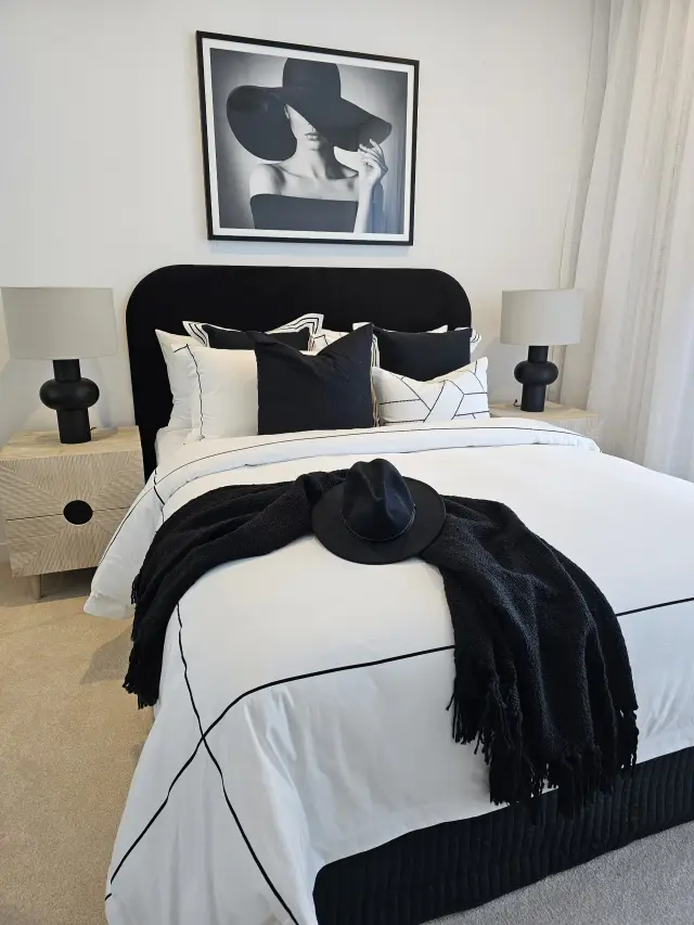 Bedroom with black velvet bedhead, black-and-white linen, timber bedsides and sculptural lamps