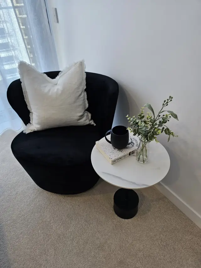 Black velvet swivel armchair with fringed linen cushion and marble side table by sheer curtains