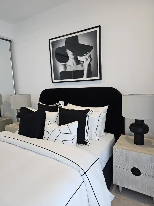 Black bedhead with layered black-and-white cushions, textured bedsides and sculptural black lamp
