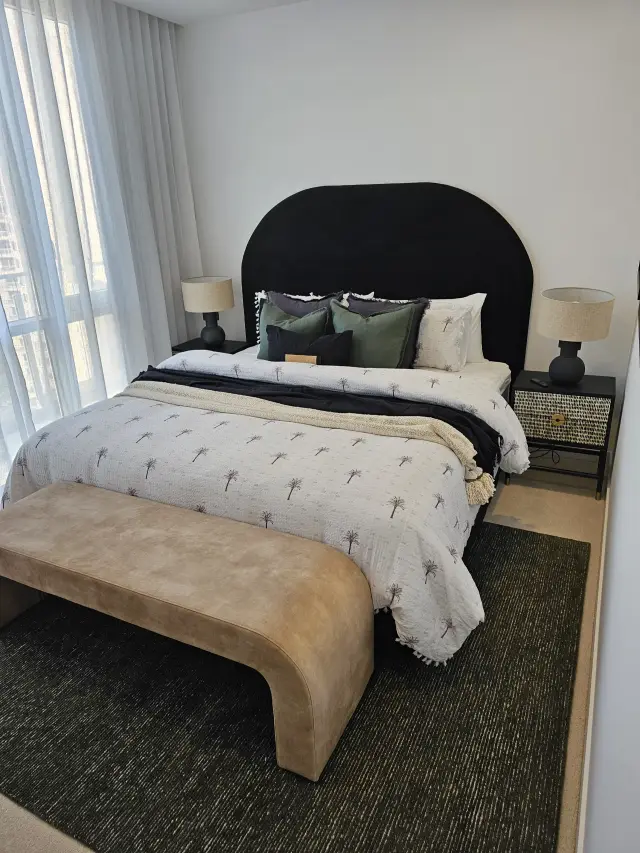 Bedroom with black arched bedhead, palm-print bedding and curved tan suede bench