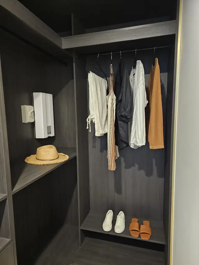 Walk-in wardrobe in dark timber with hanging resortwear, straw hat and shoe shelf