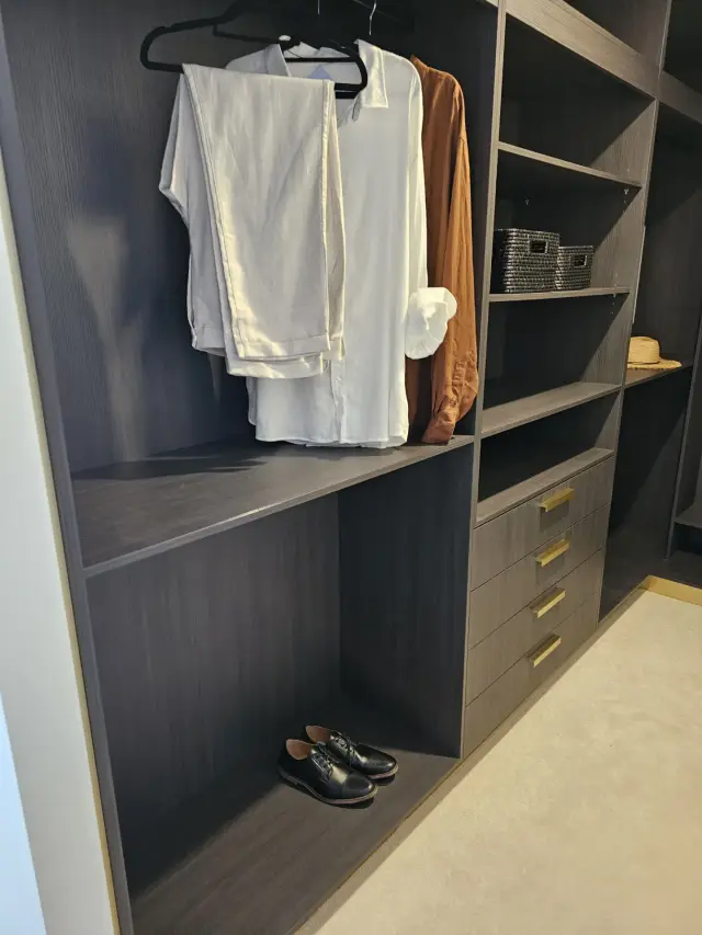 Dark timber wardrobe with folded linen, brass-handled drawers and woven storage baskets
