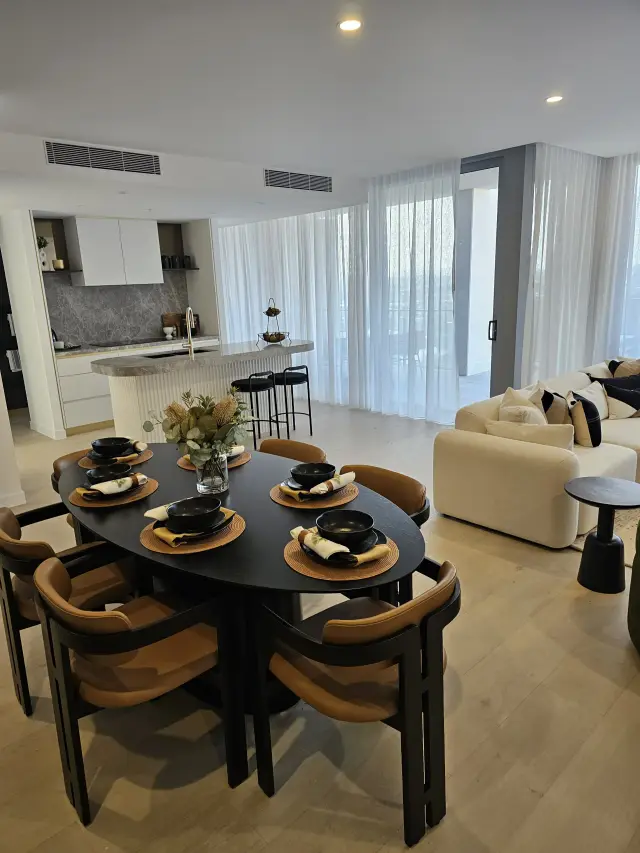 Open-plan dining and living with black oval table, tan leather chairs and cream sofa