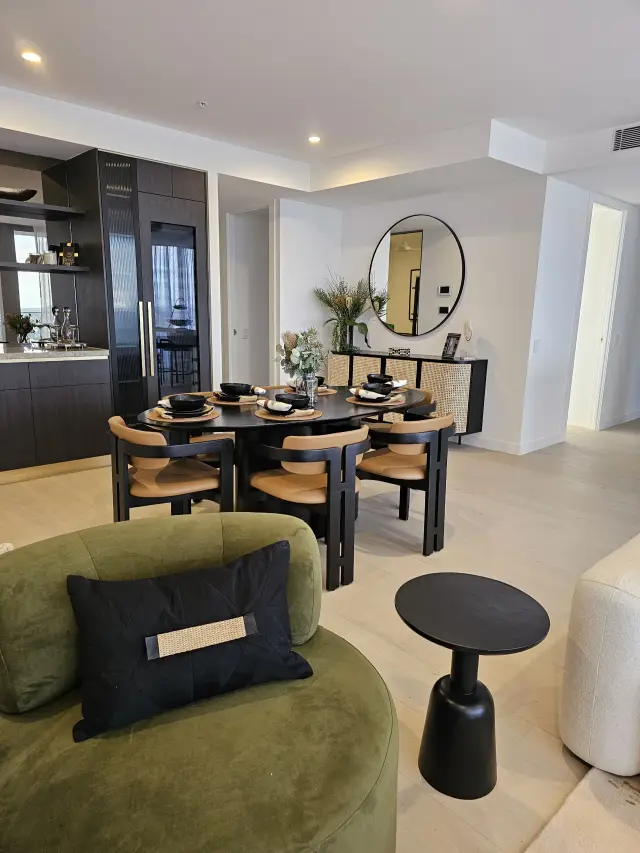 Dining area with black oval table, tan chairs, rattan sideboard and round mirror