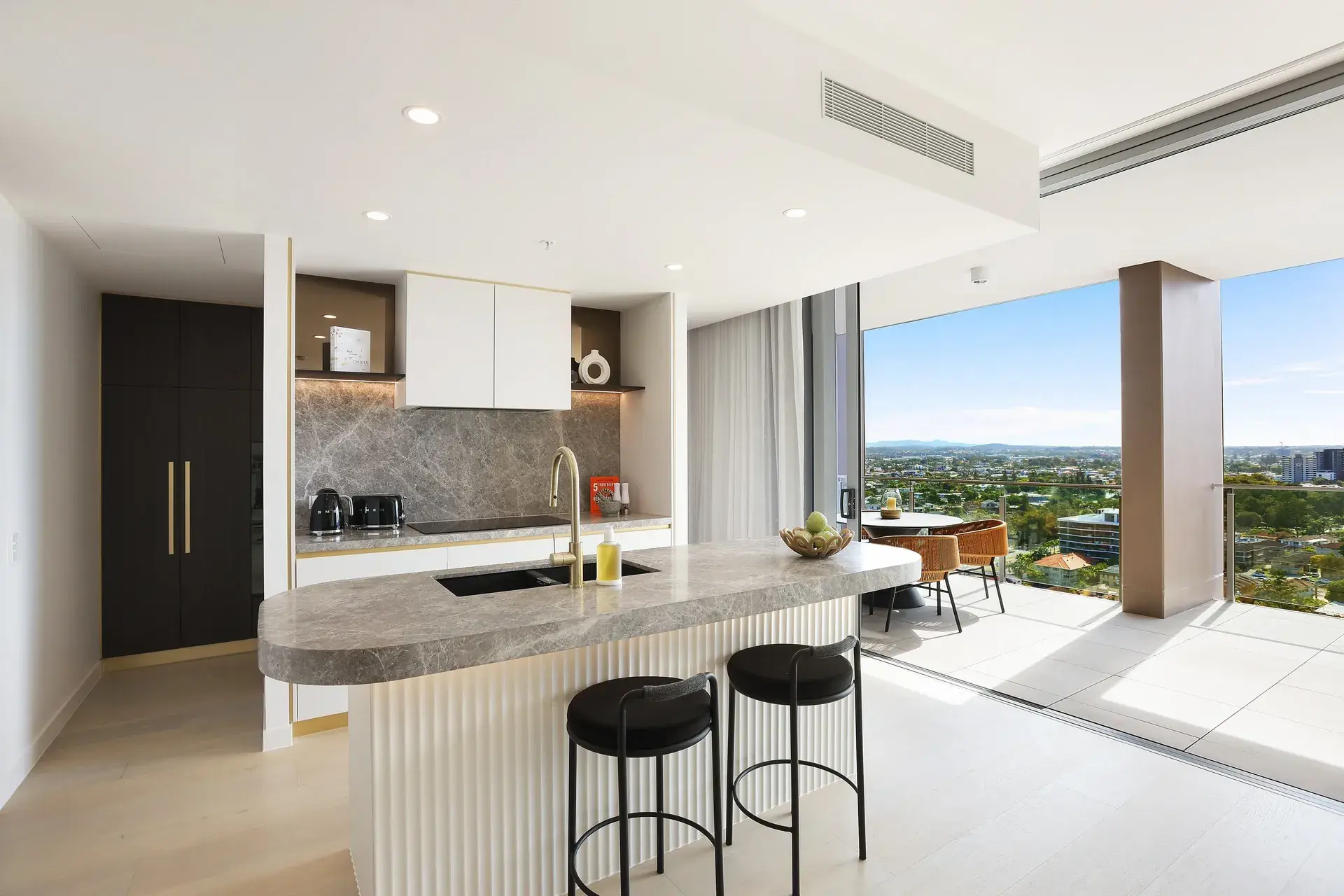 Kitchen with grey marble island and black bar stools opening to a terrace with hinterland views