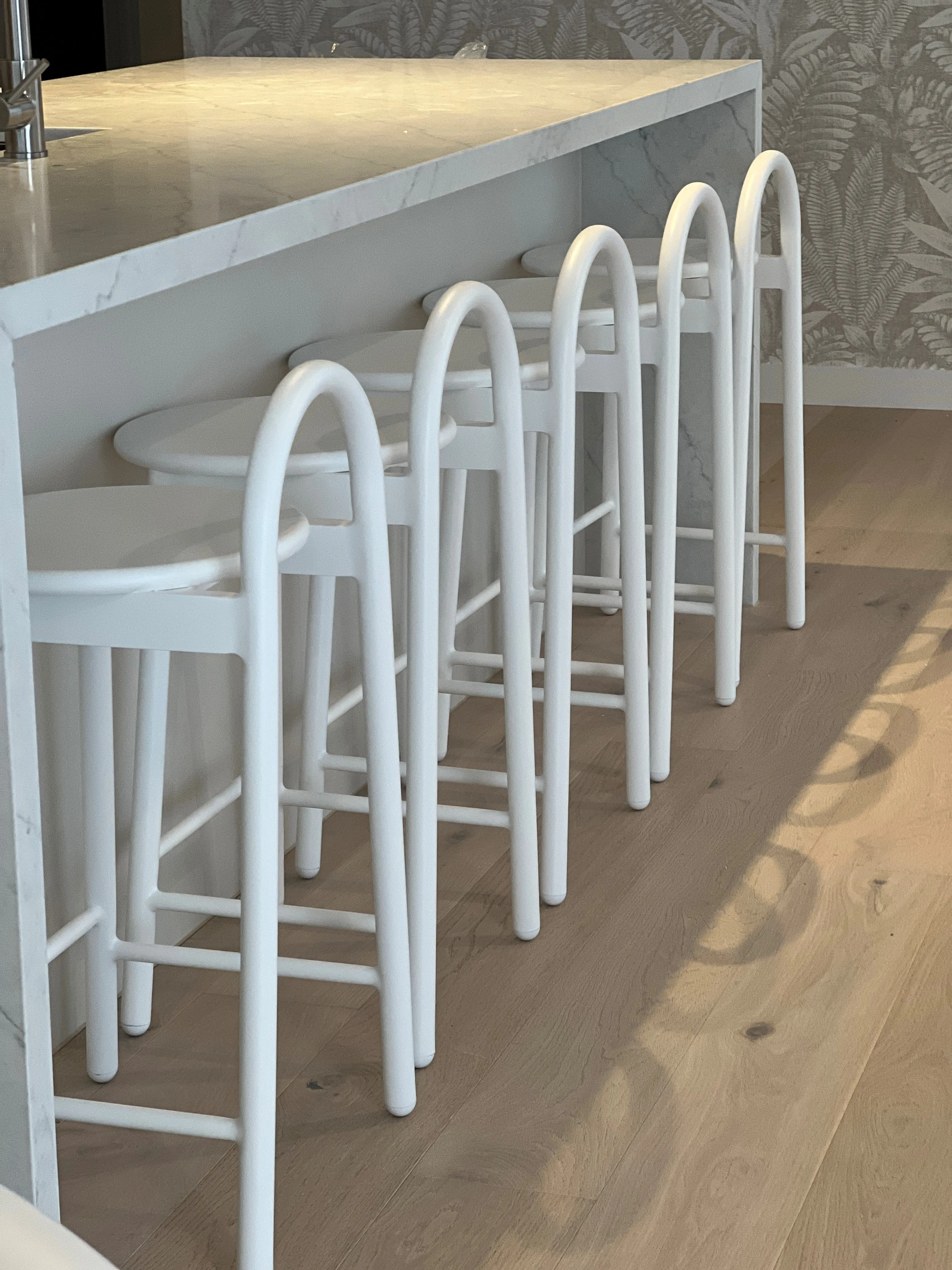 Kitchen island with marble benchtop and white arched bar stools on oak flooring