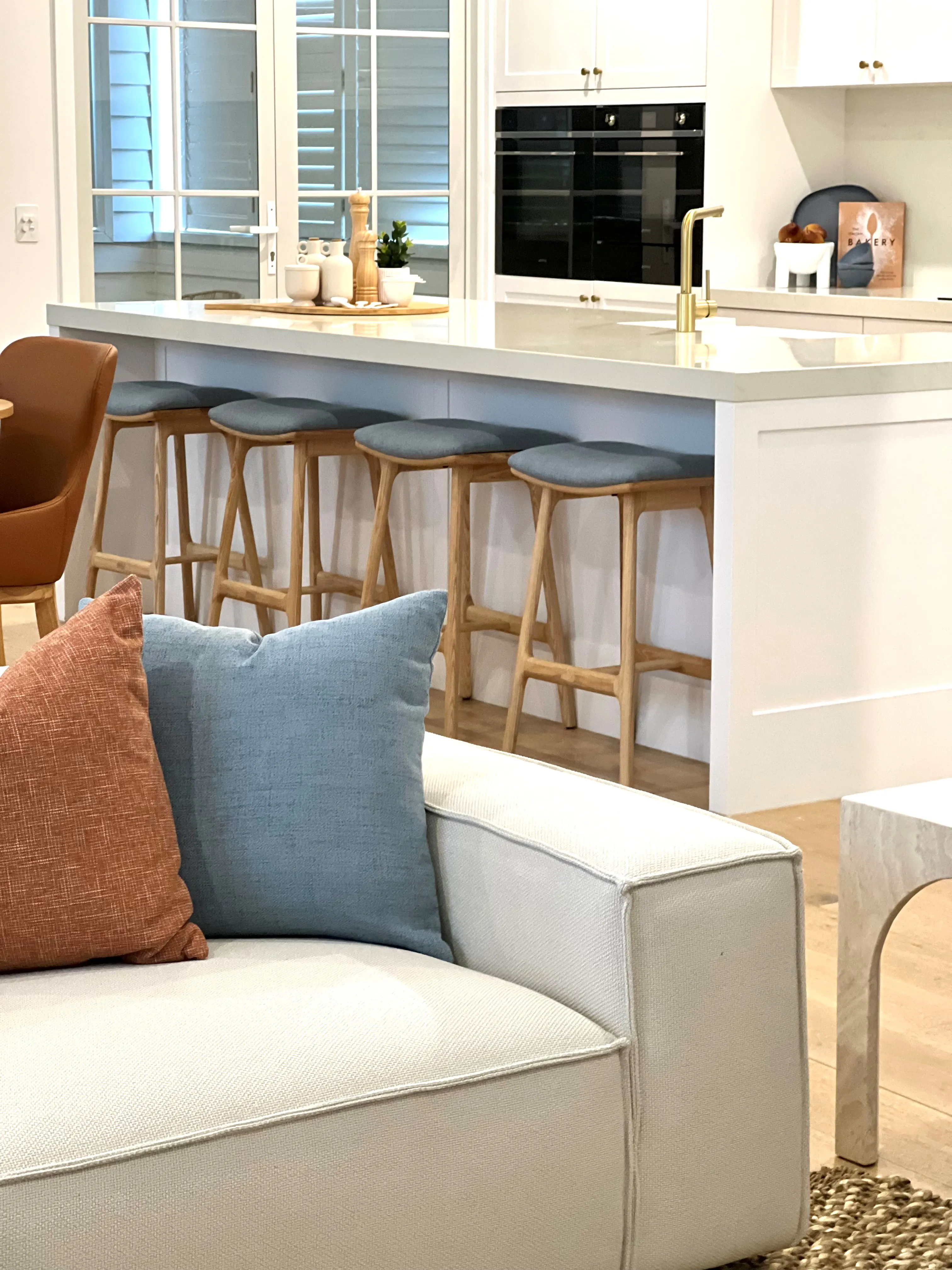 White kitchen with blue-seated oak bar stools, brass tapware and stone benchtop