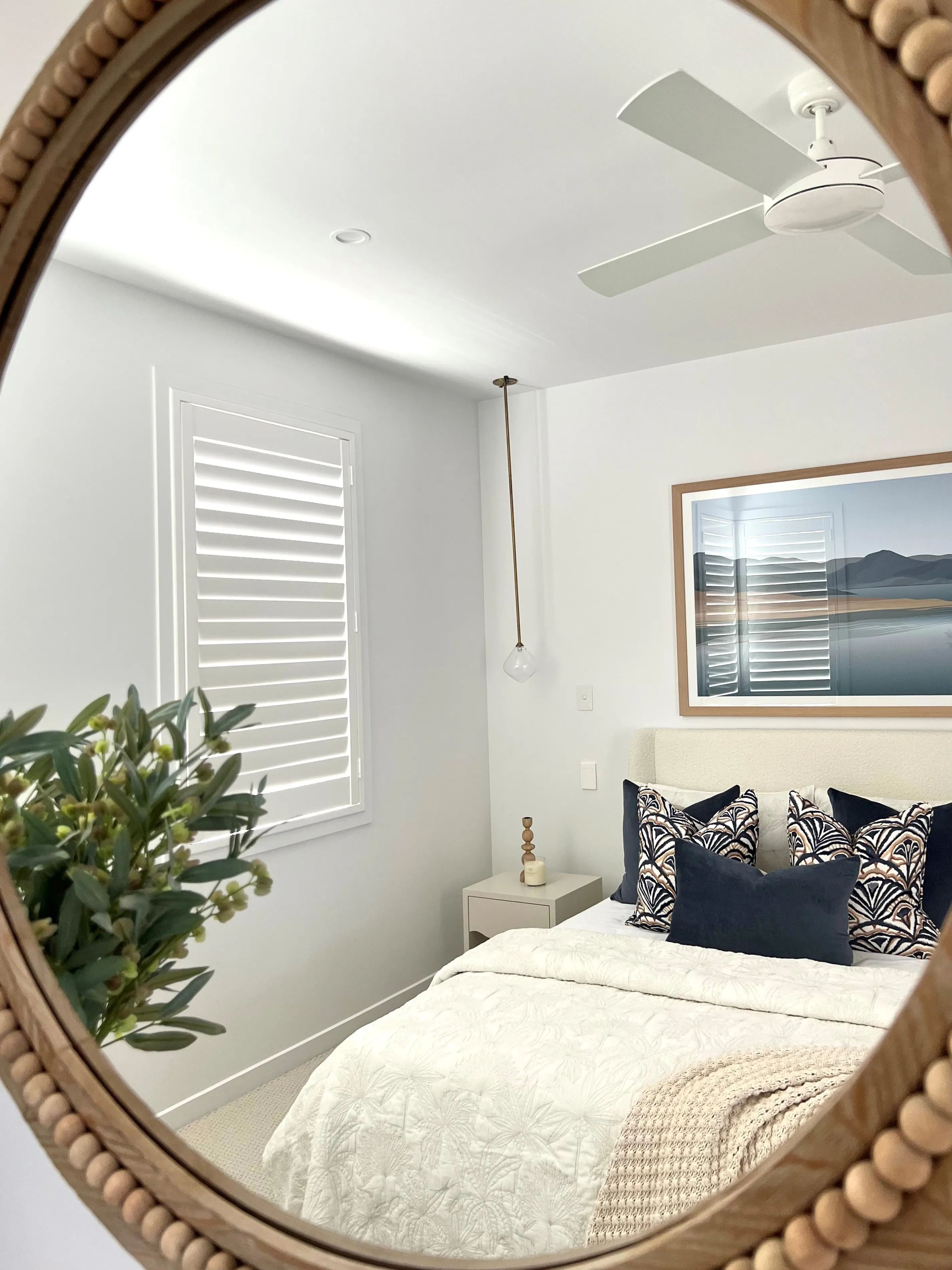 Master bedroom with beaded rope round mirror, plantation shutters and navy palm-print cushions