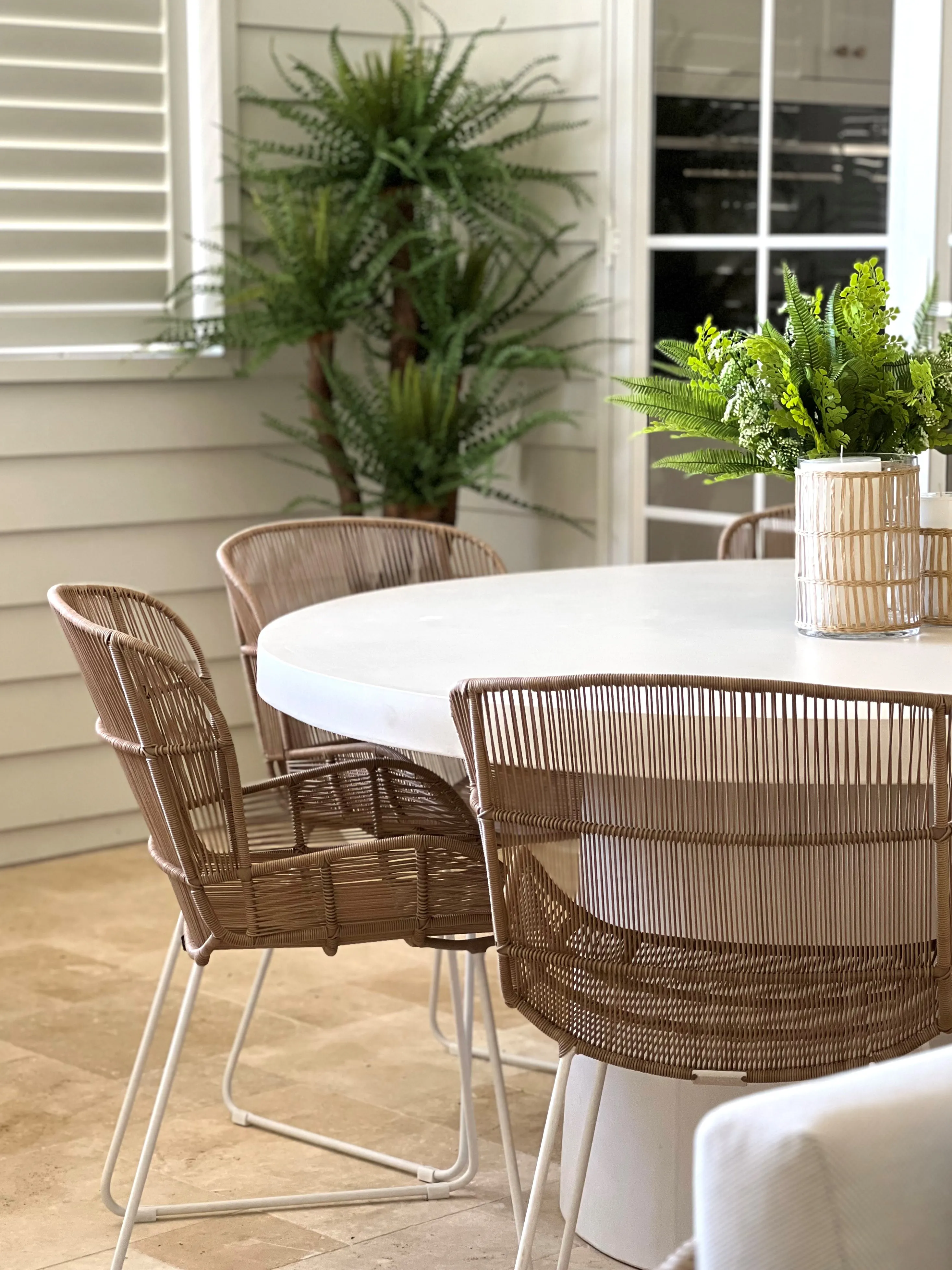 Outdoor entertaining area with rope-woven dining chairs, white table and tropical ferns