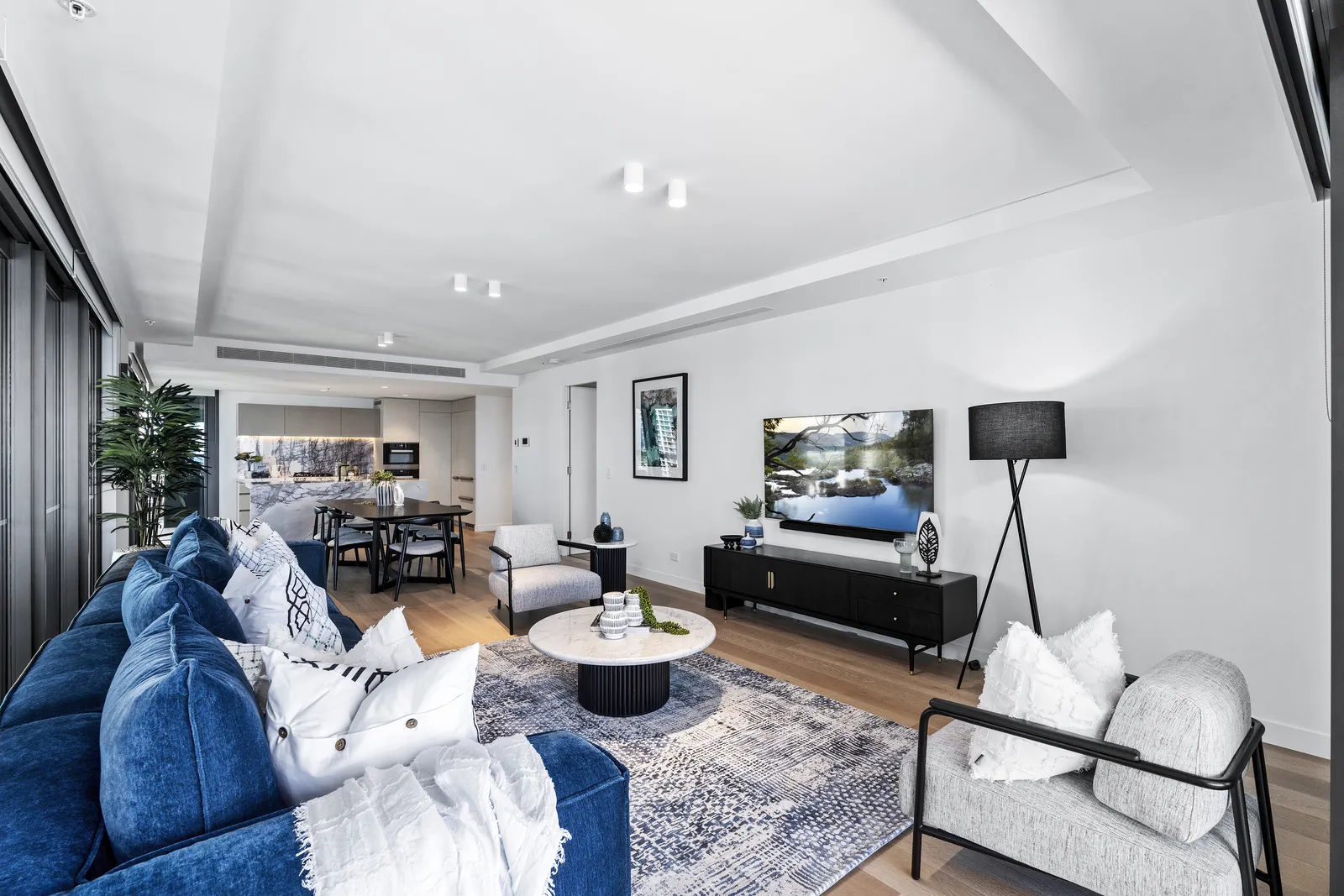 Second apartment living area with blue sofa, white armchair and black entertainment unit