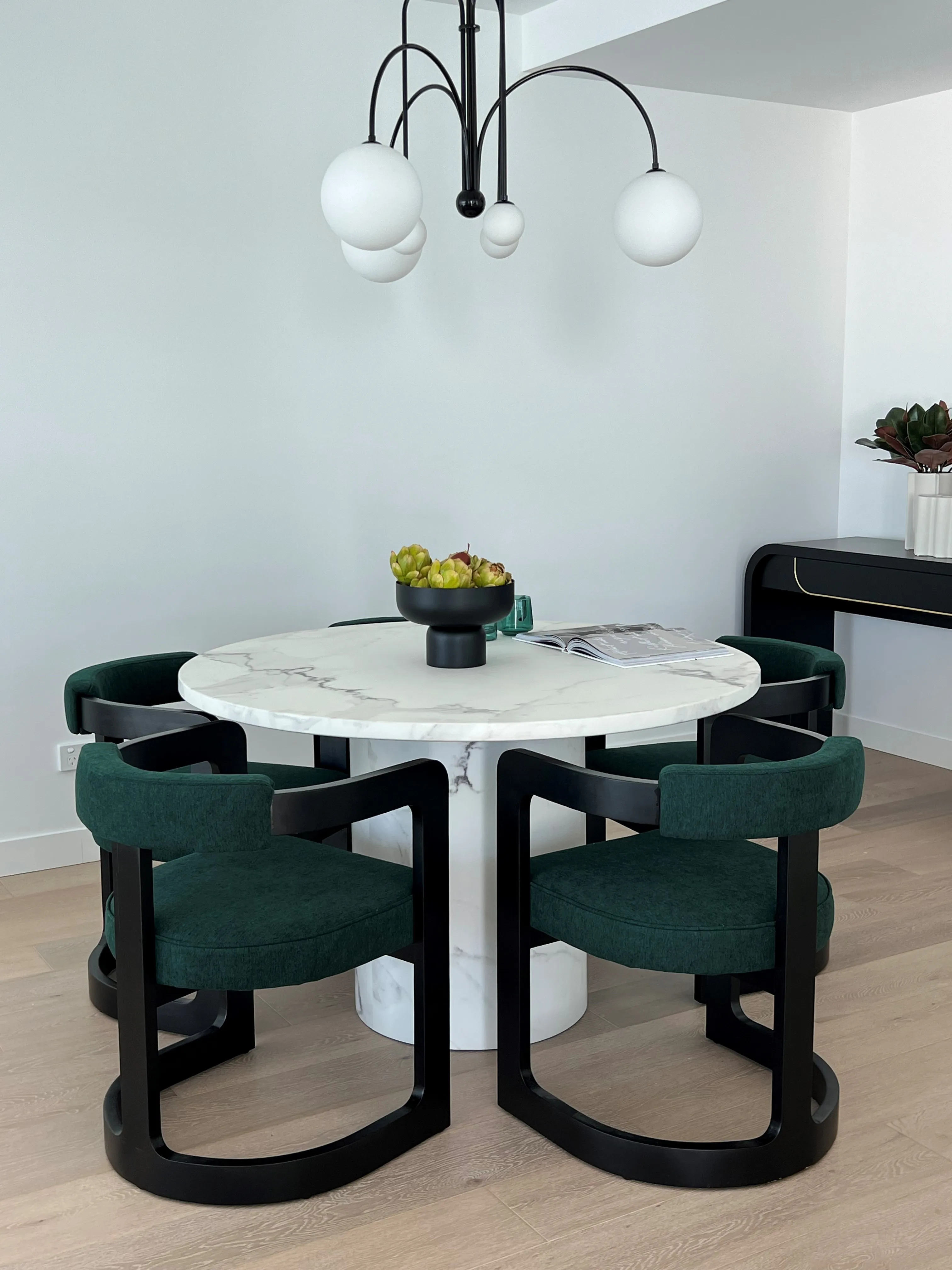 Round marble dining table with emerald upholstered chairs and black globe chandelier