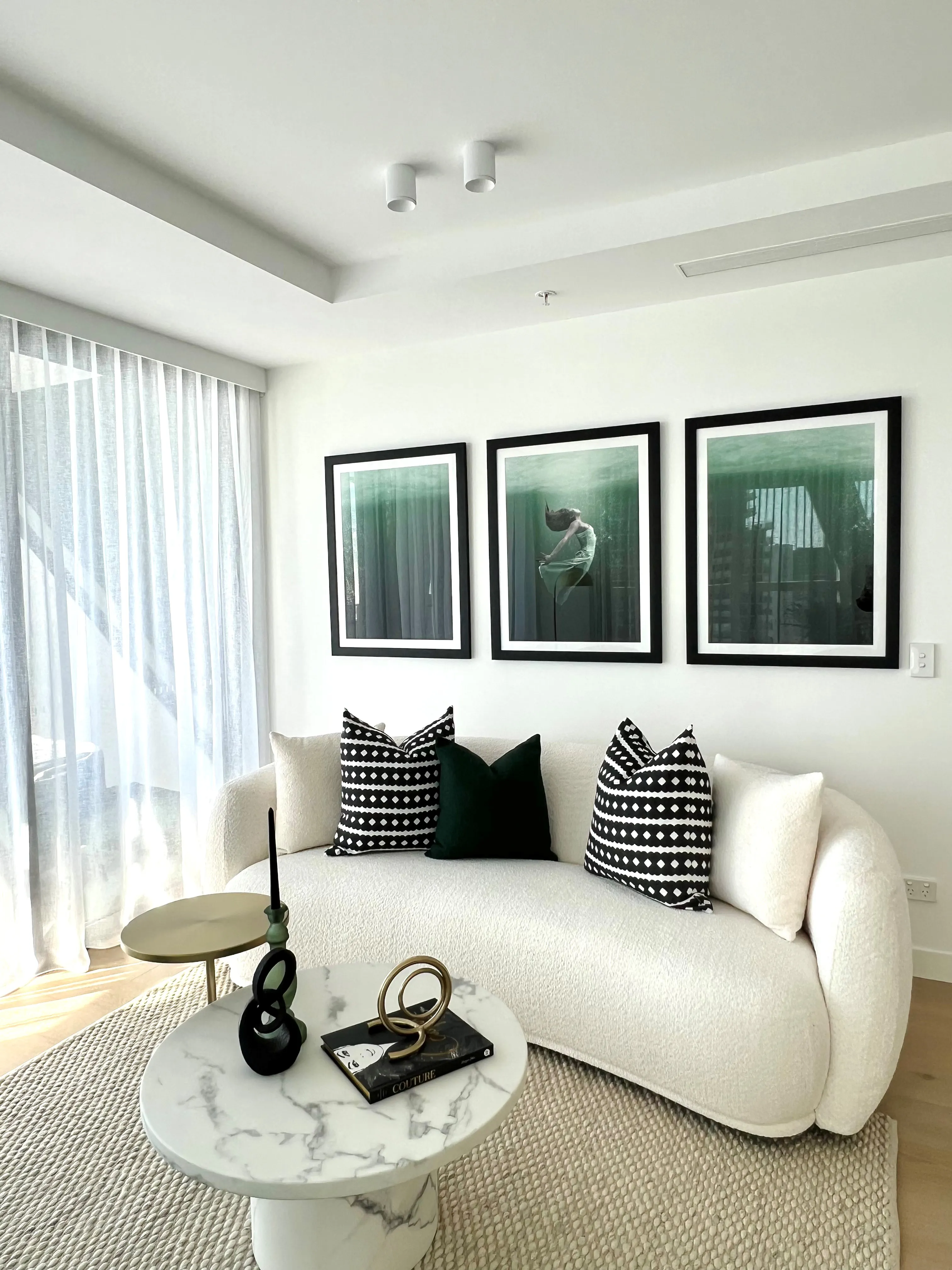 Cream bouclé curved sofa with monochrome cushions, marble side table and teal artwork triptych