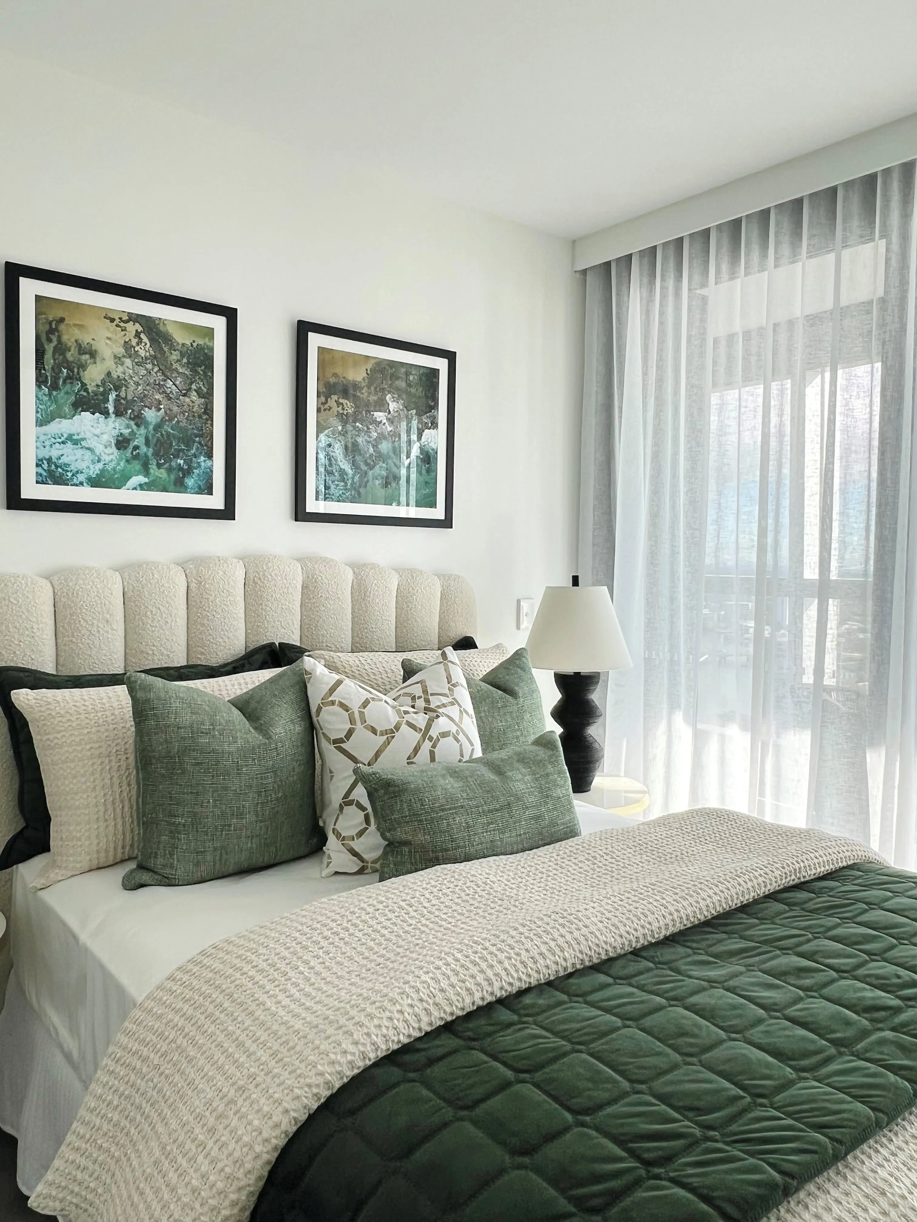 Bedroom with channel-tufted cream bedhead, emerald velvet cushions and botanical artwork