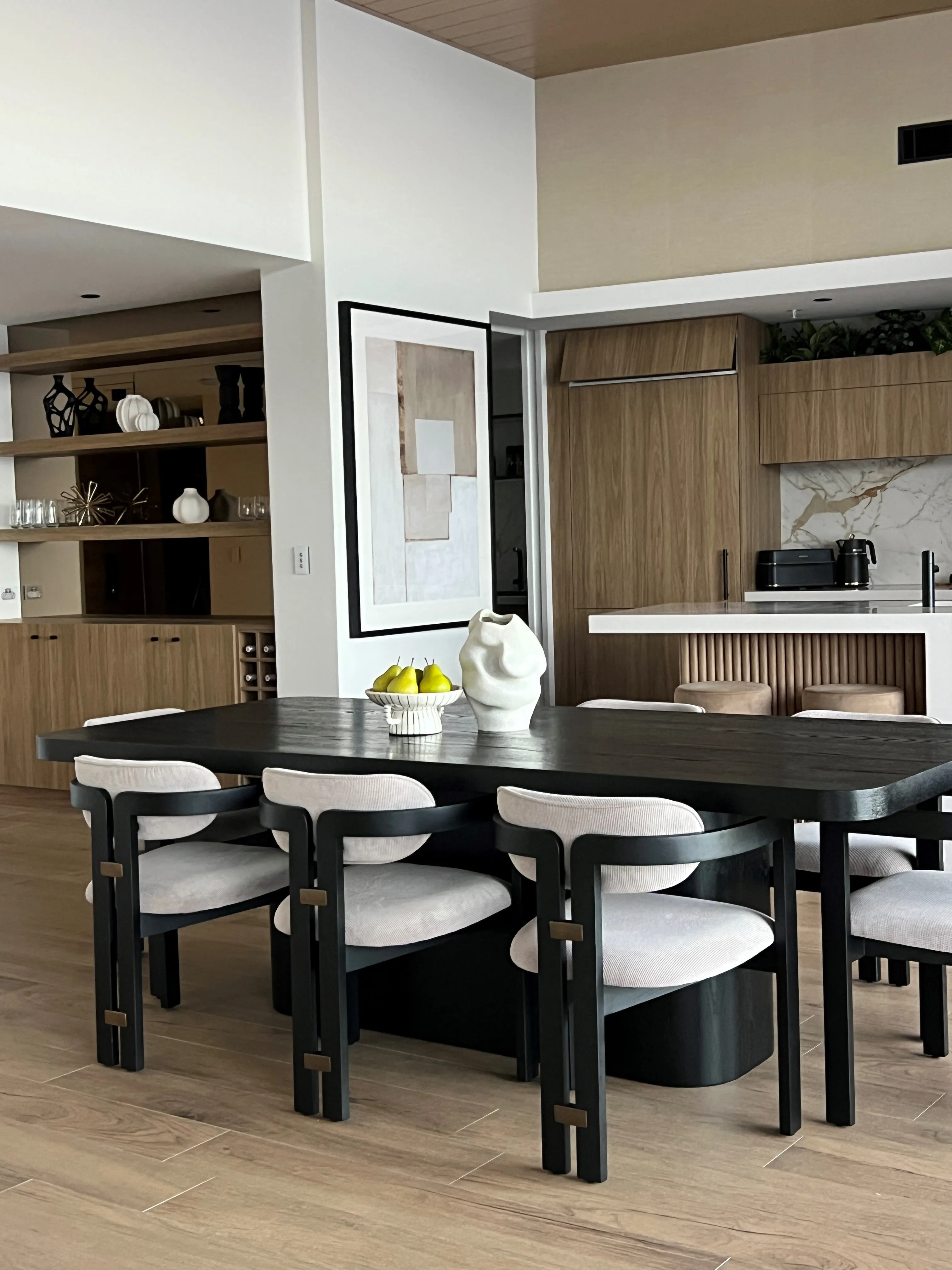 Dining area with black sculptural table, cream upholstered chairs and fluted oak kitchen beyond