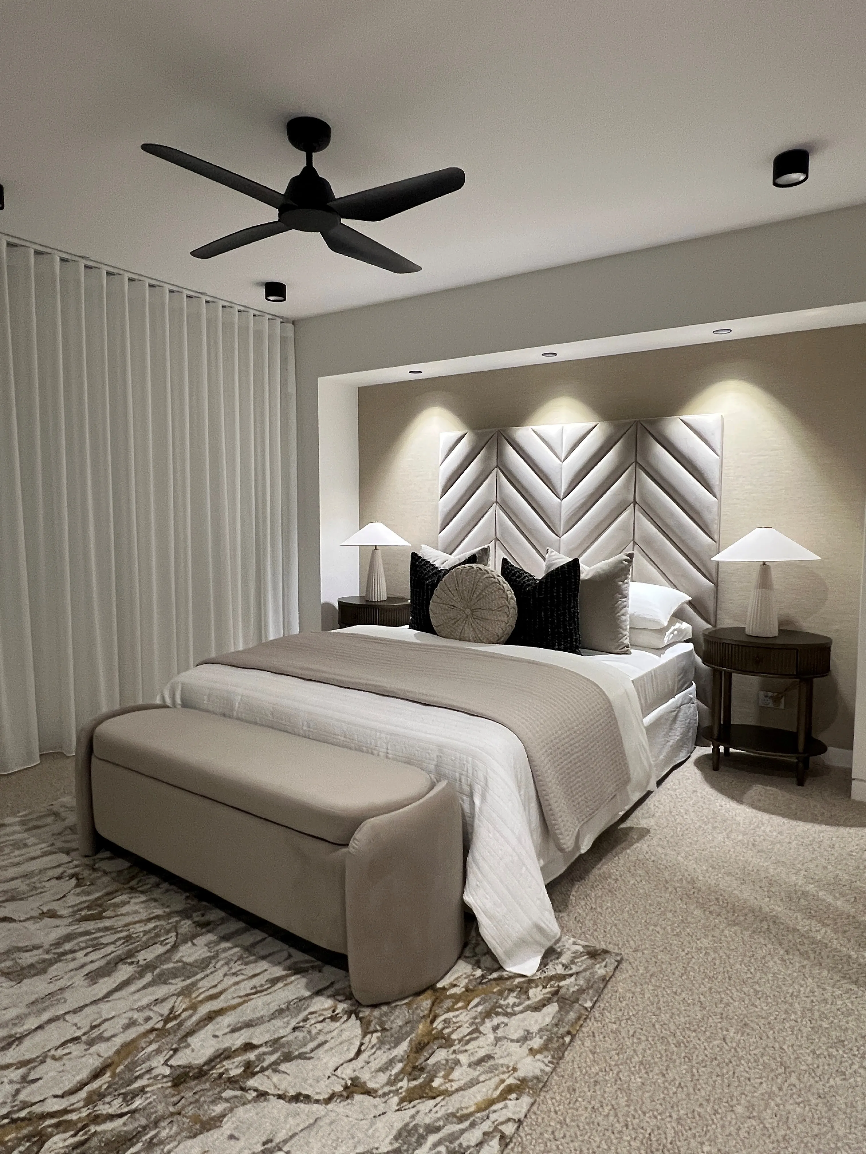 Master bedroom with chevron upholstered bedhead, taupe linen bedding and marble-pattern rug
