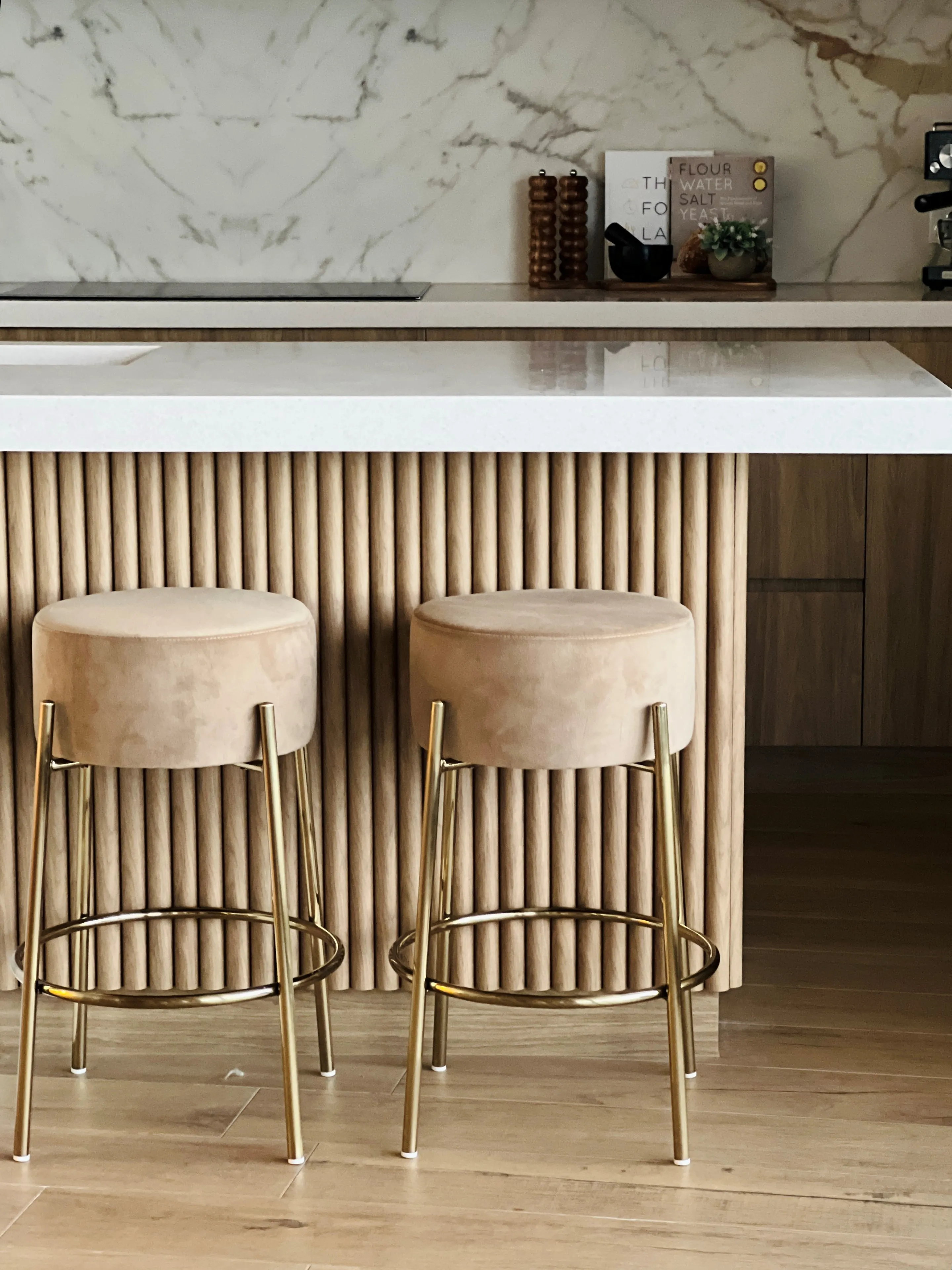 Kitchen island detail with suede bar stools on brass legs and fluted oak panelling