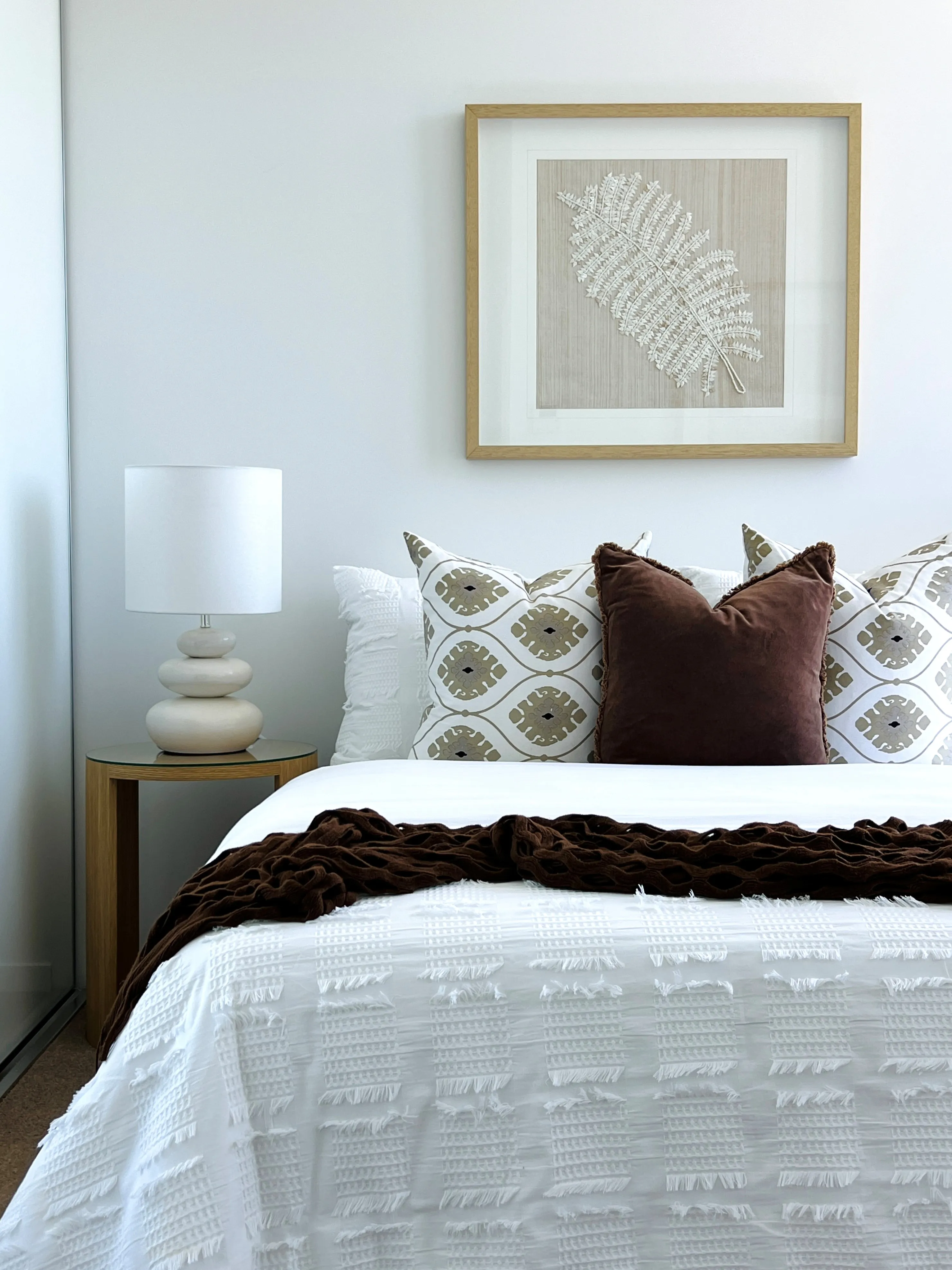 Master bedroom with white waffle bedding, chocolate velvet cushion and pressed fern artwork