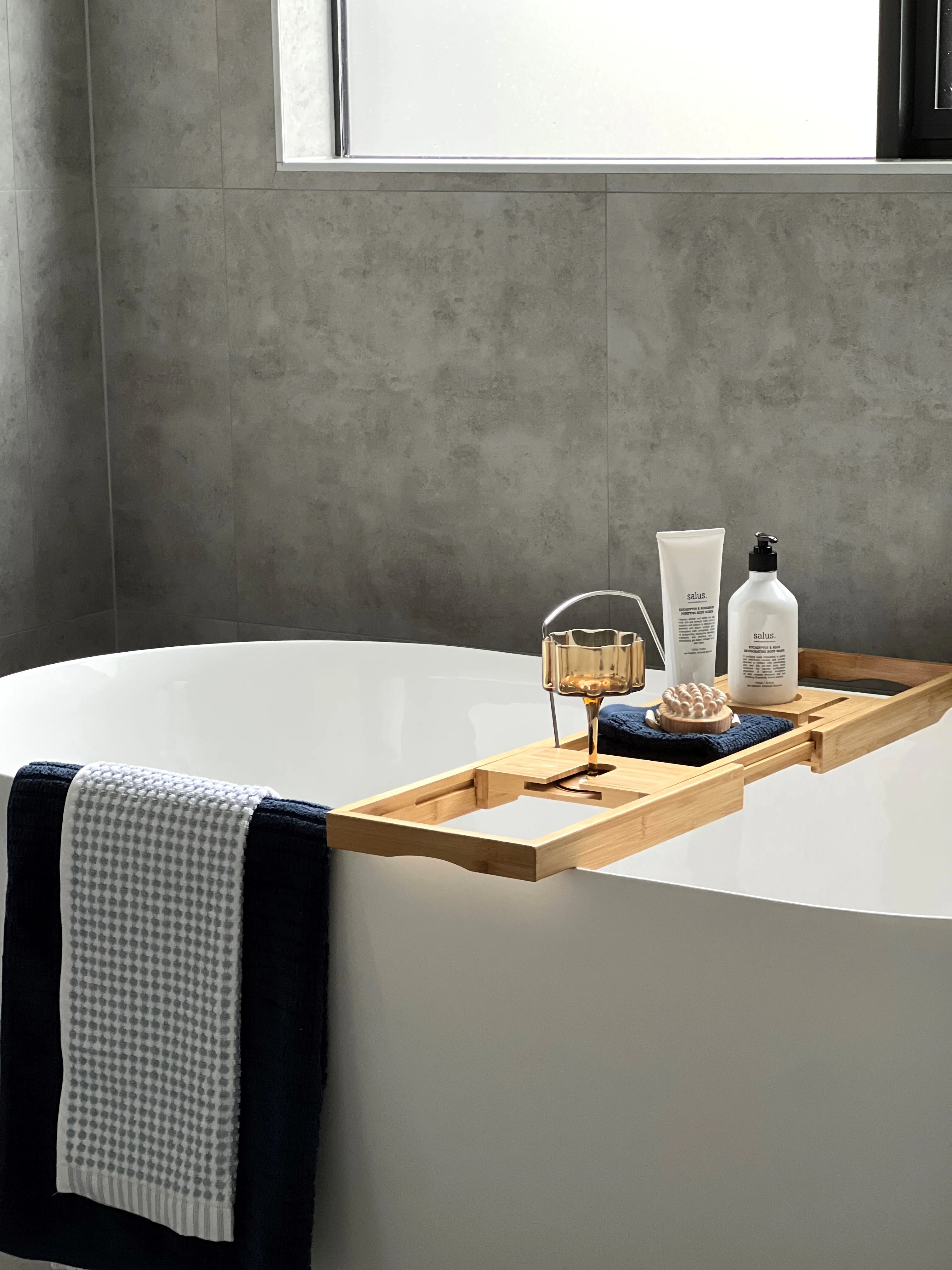 Freestanding white bathtub with bamboo bath caddy against grey stone tiles