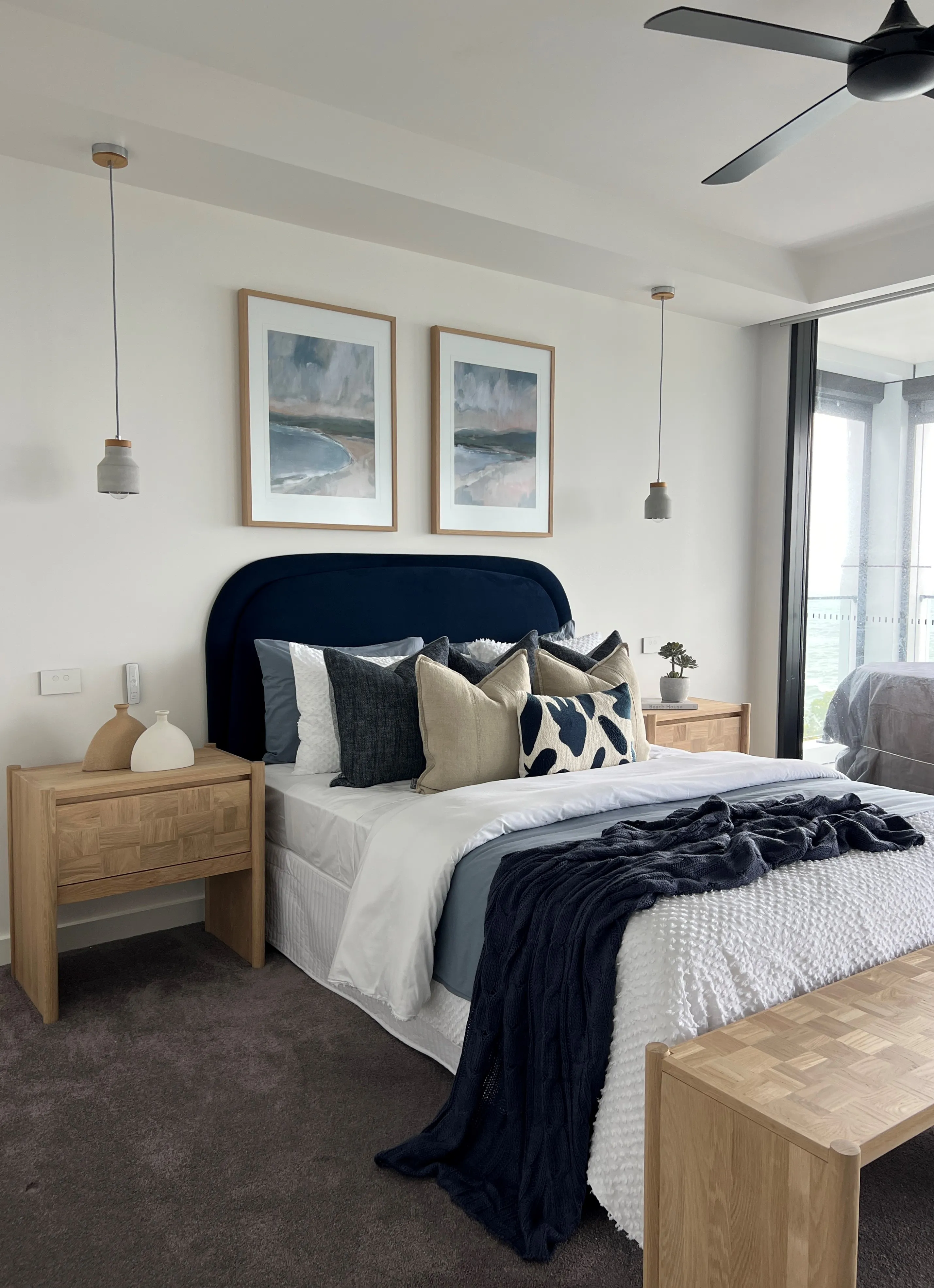 Master bedroom with navy upholstered bedhead, oak bedsides and coastal diptych artwork