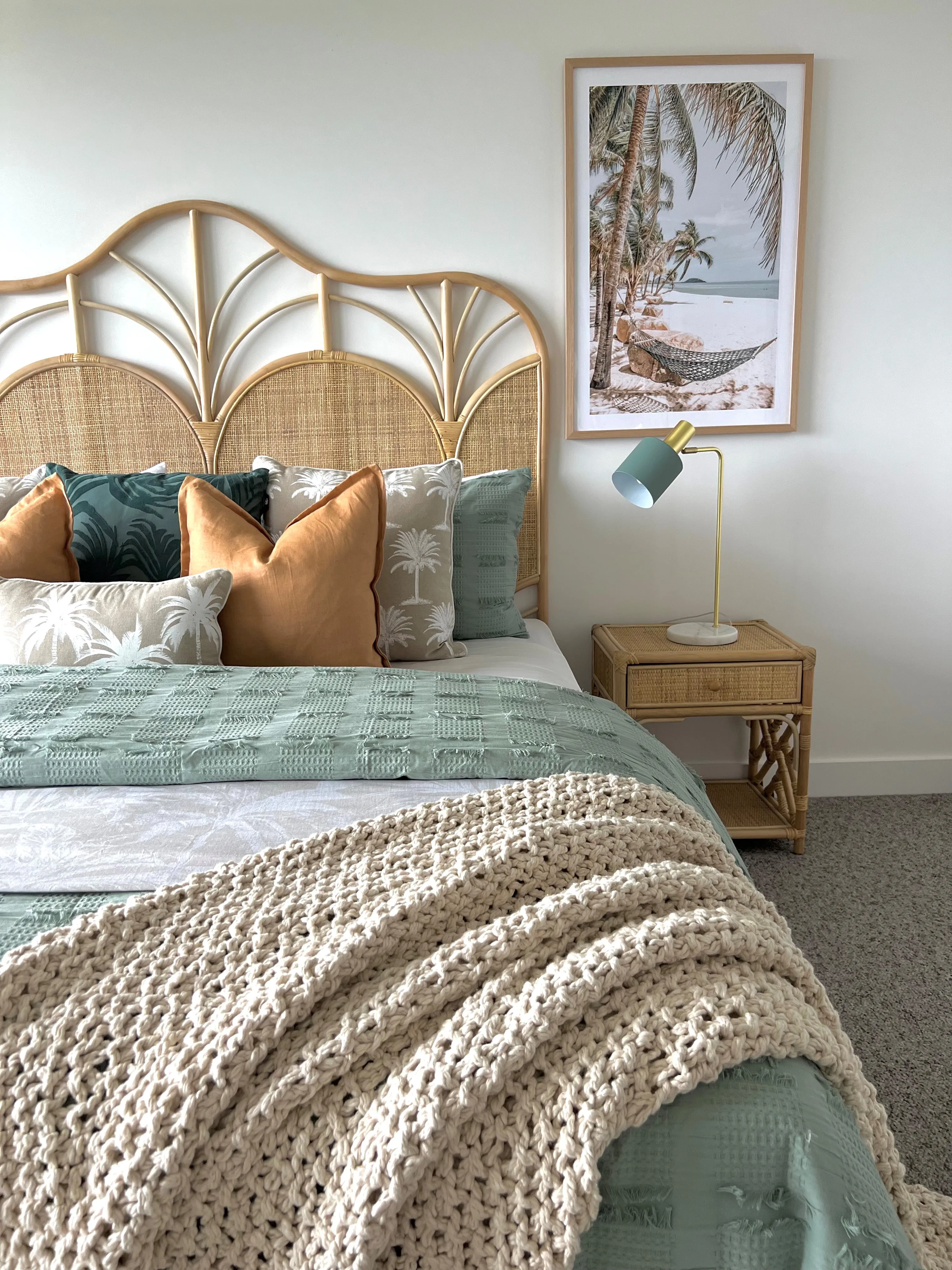 Bedroom with arched rattan bedhead, sage and terracotta cushions and tropical hammock artwork