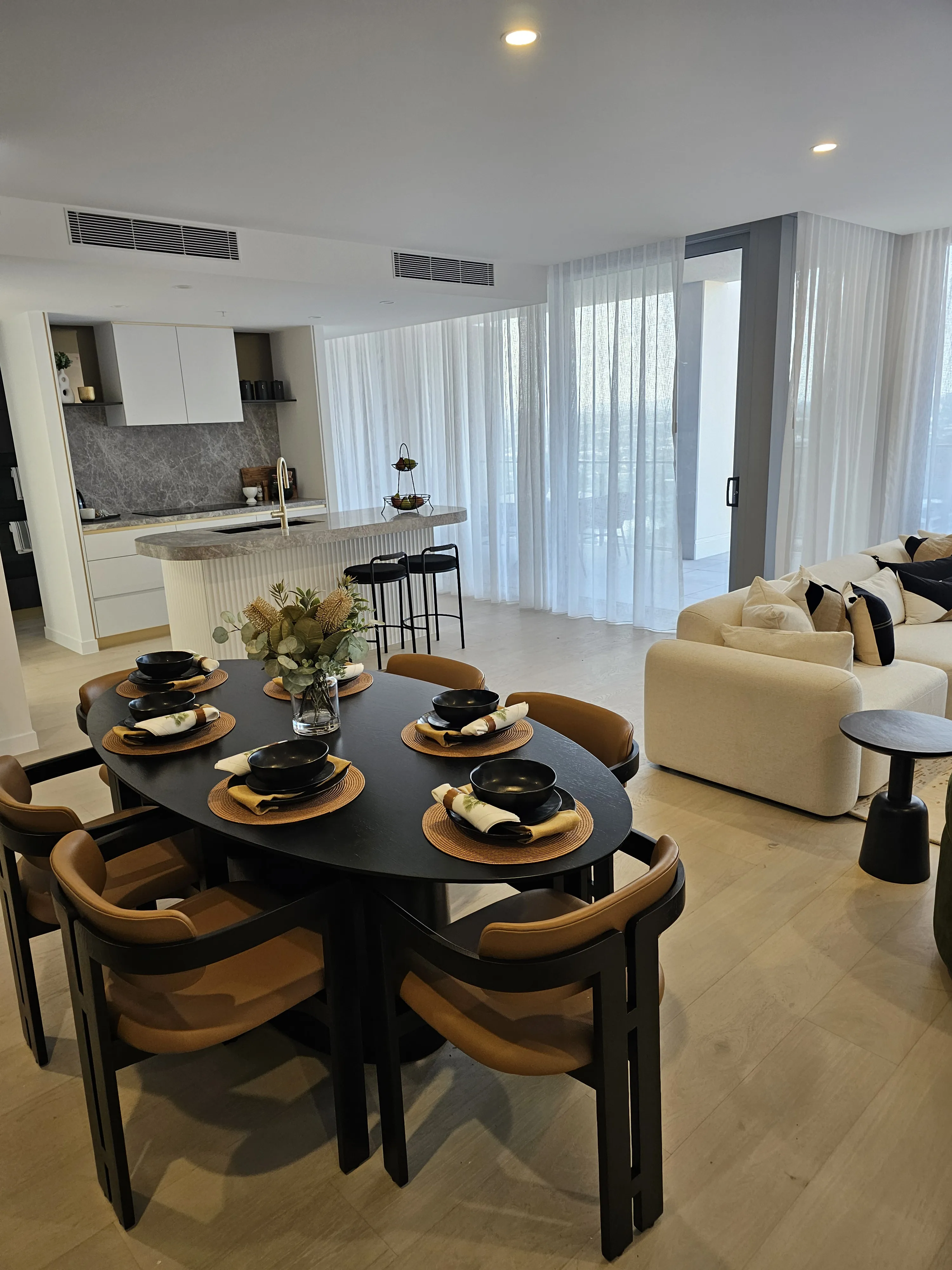 Open-plan dining with black oval table, tan leather chairs and fluted kitchen island