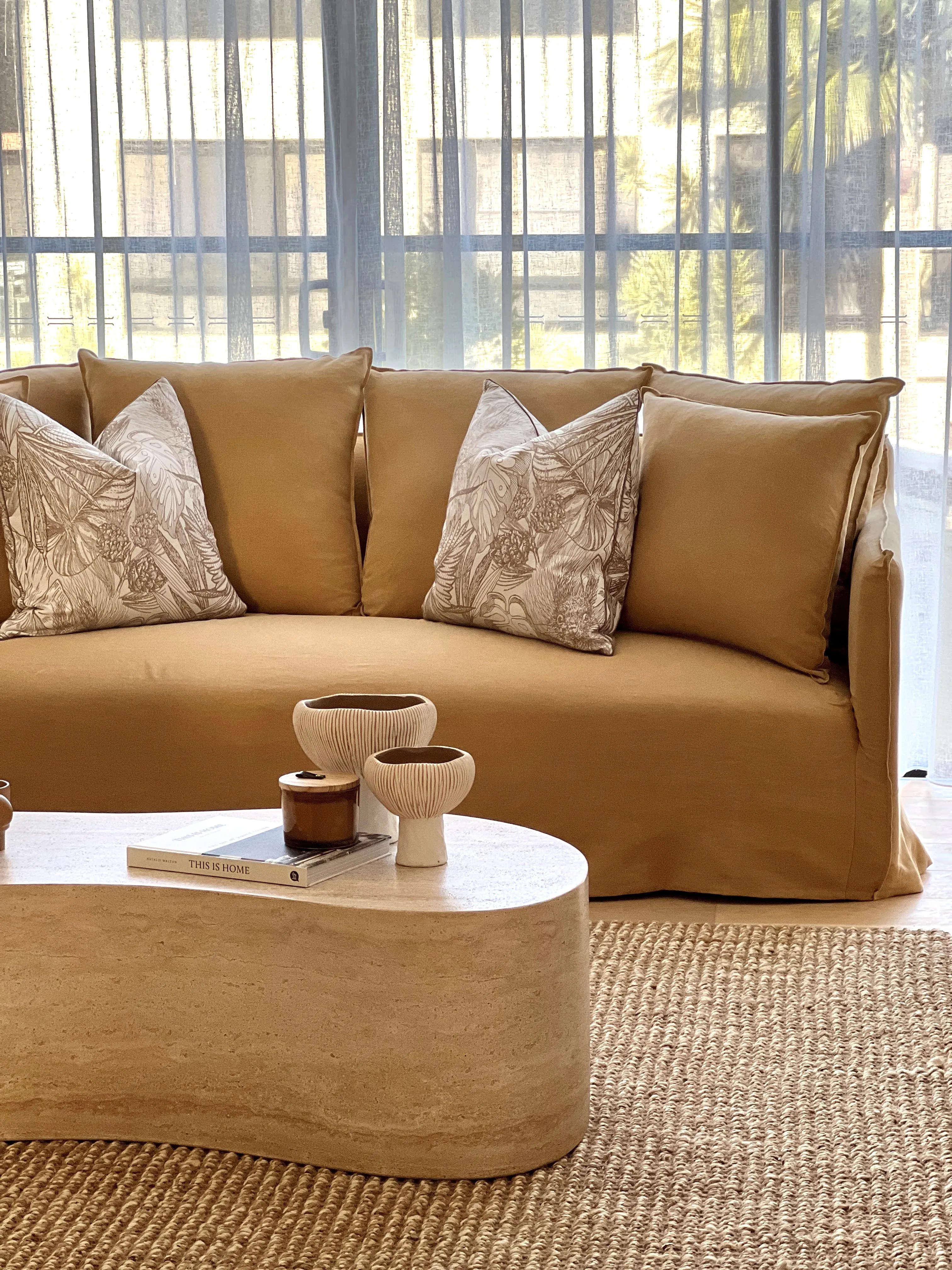 Tan linen sofa with botanical cushions and travertine coffee table on jute rug