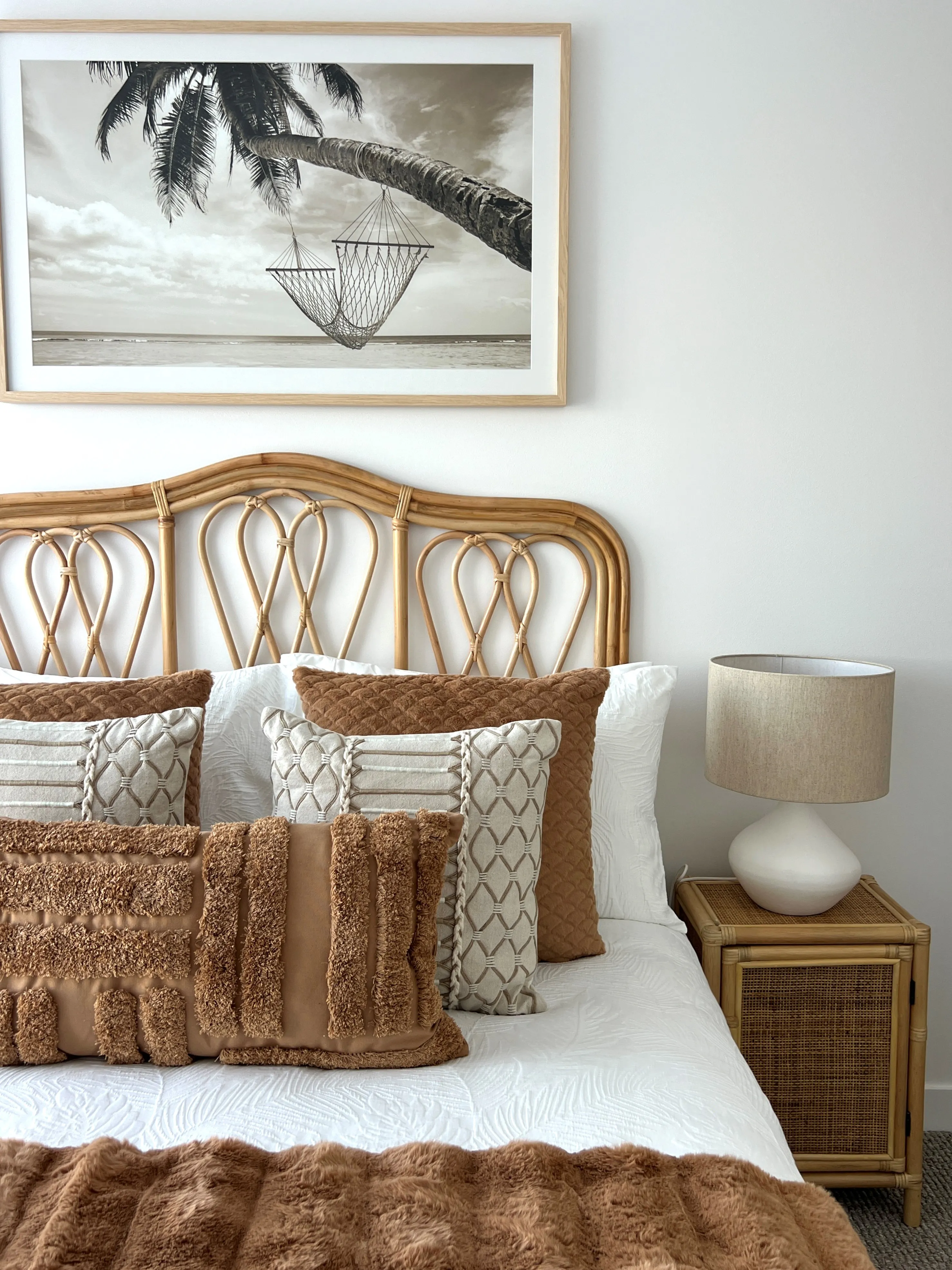 Master bedroom with rattan bedhead, tan textured cushions and coastal photography